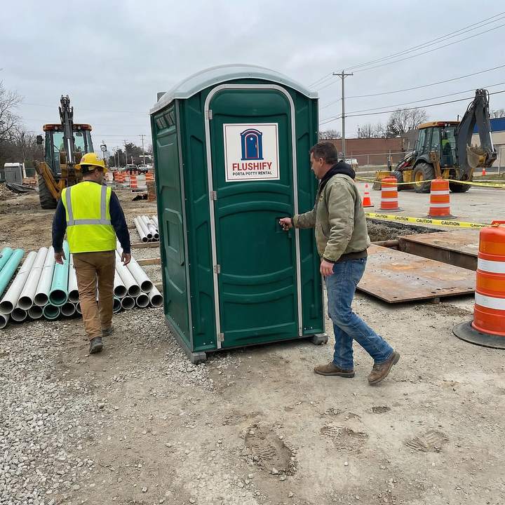 Green portable toilet on a construction site with an excavator behind it