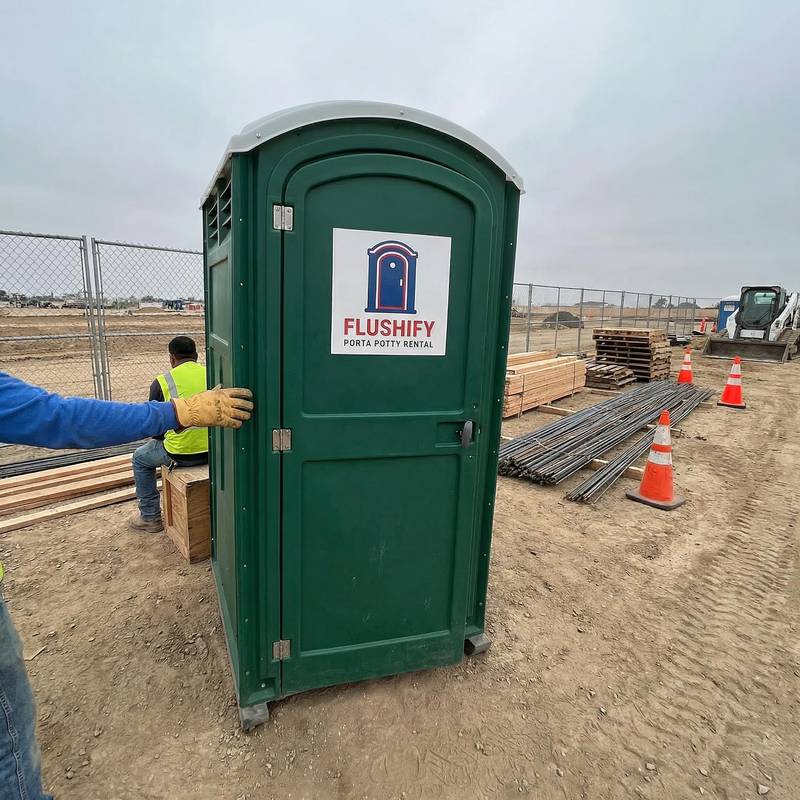 Green portable toilet at a construction site with rebar stacked nearby